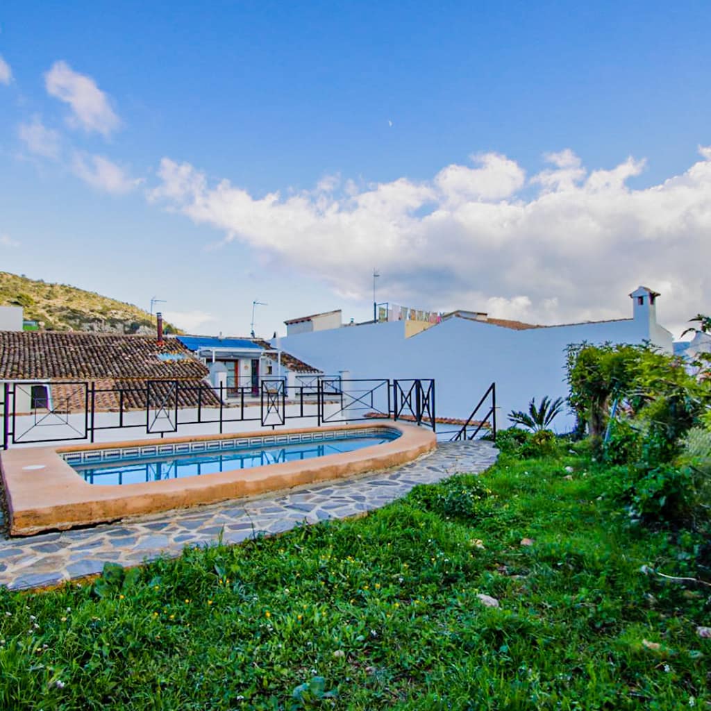 Private outdoor pool at Casa 45 in Tàrbena, surrounded by a stone terrace, garden greenery, and traditional village rooftops under a blue sky.